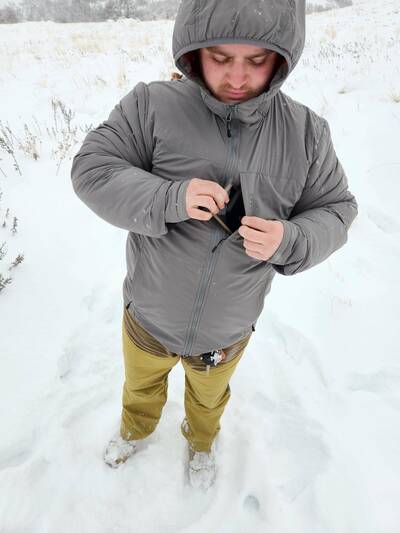 Man in Orvis Pro Insulated Hoodie in snow putting phone away